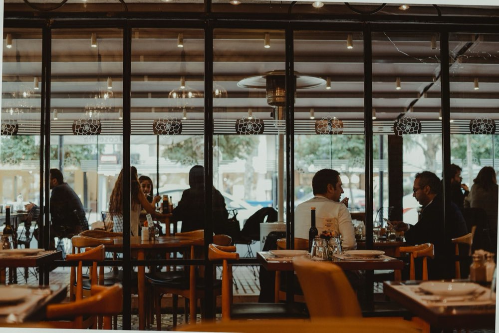 Clientes sentados às mesas de um restaurante, um deles usando o celular